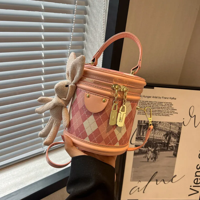 Textured rhombus cylindrical PU bucket bag in beige with white rabbit pendant, 14 cm wide.