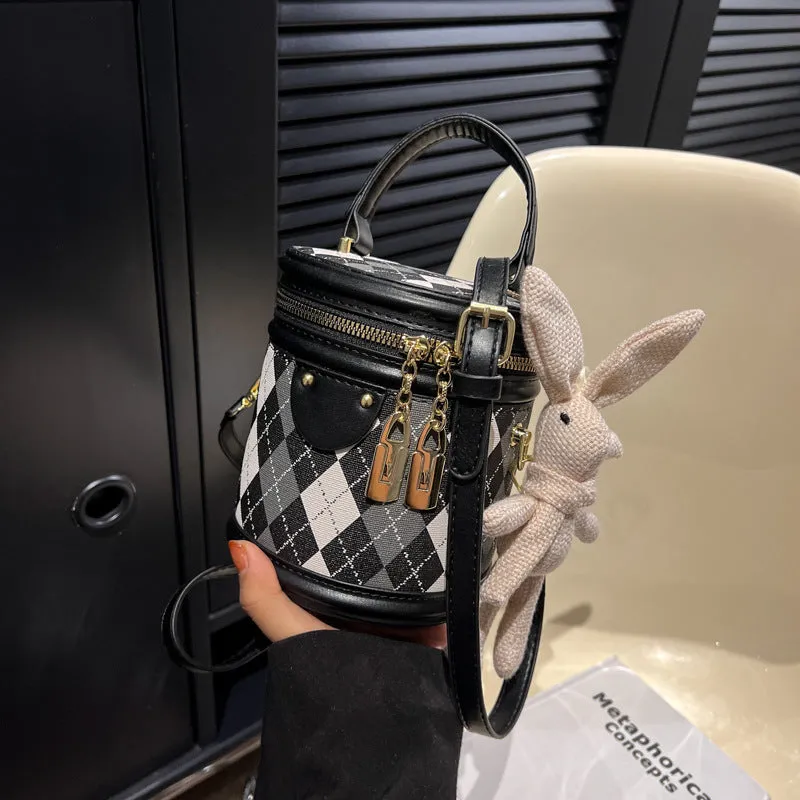 Textured rhombus cylindrical PU bucket bag in beige with white rabbit pendant, 14 cm wide.