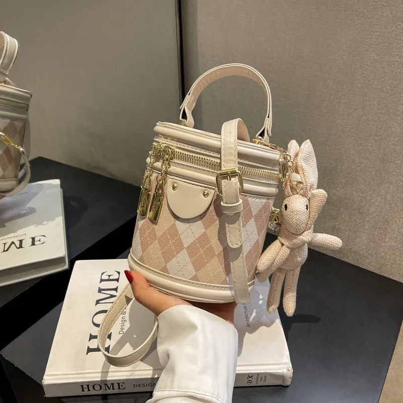 Textured rhombus cylindrical PU bucket bag in beige with white rabbit pendant, 14 cm wide.