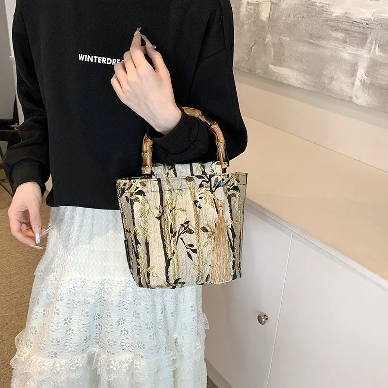 Beige polyester women's handbag with bamboo handles and pendant on neutral background