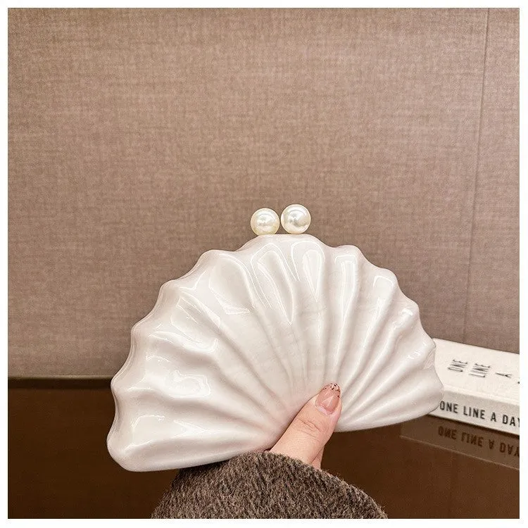 Acrylic shell-shaped clutch bag in champagne with silver chain on white background