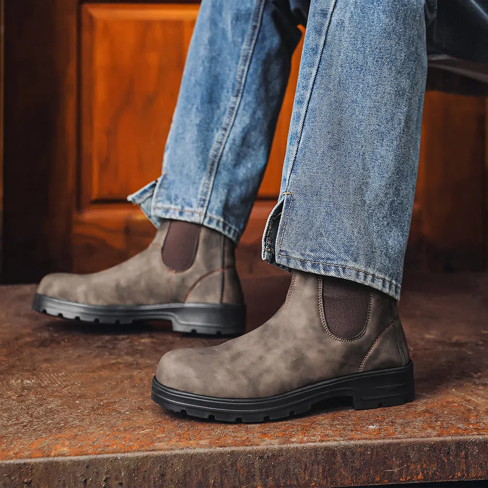 Chelsea boots in black with low wedge heel, round toe, and mid-calf shaft on a neutral background