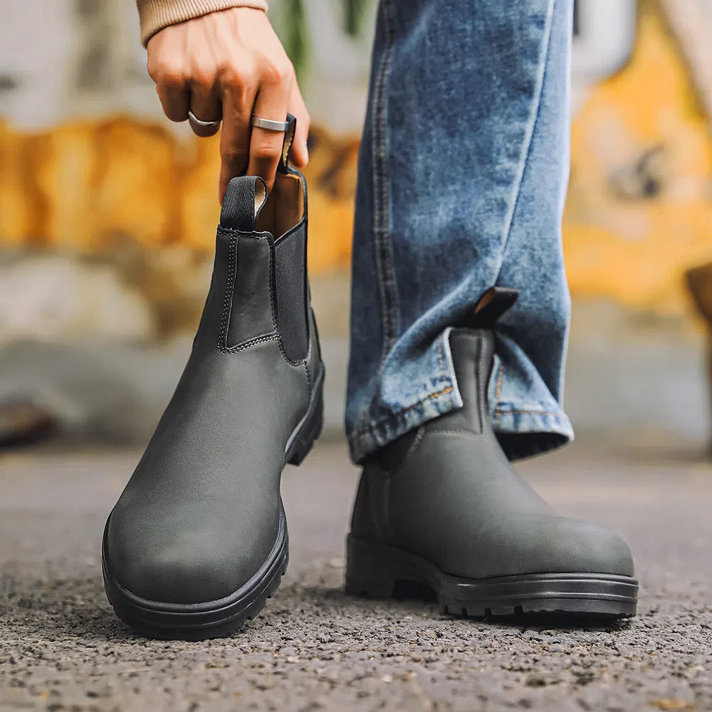 Chelsea boots in black with low wedge heel, round toe, and mid-calf shaft on a neutral background