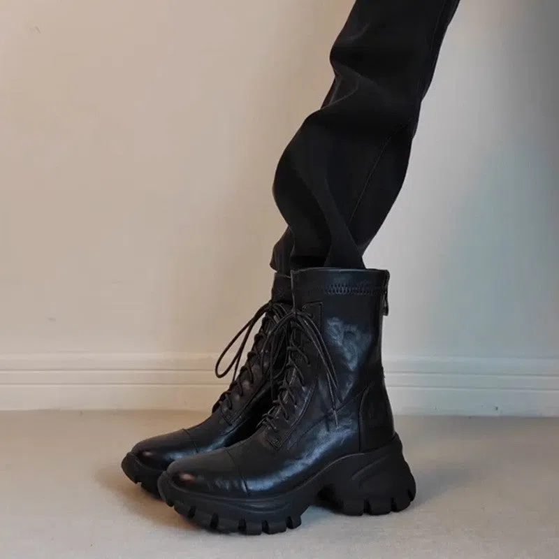 Black thick-soled motorcycle boots with back zipper and lace-up closure on a grey background