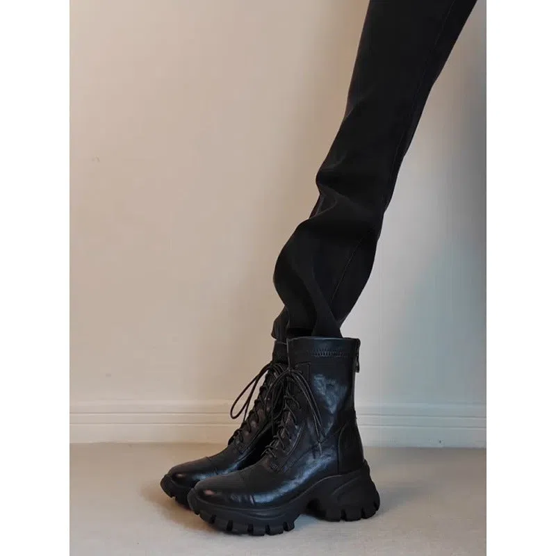 Black thick-soled motorcycle boots with back zipper and lace-up closure on a grey background
