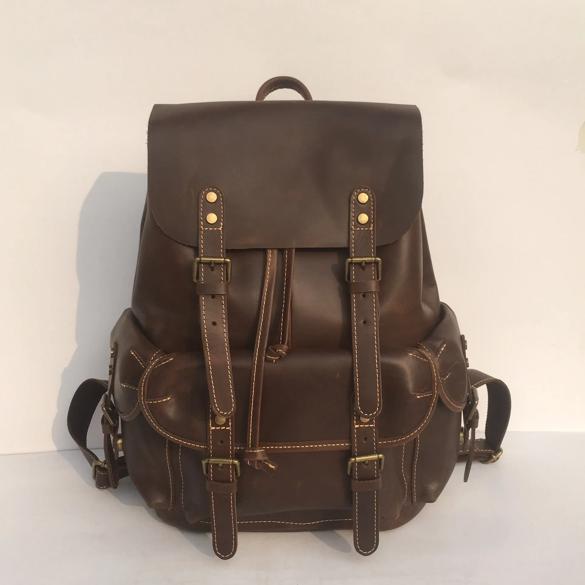 Brown men's leather backpack showing genuine cowhide material and integrated air pillow shoulder straps.
