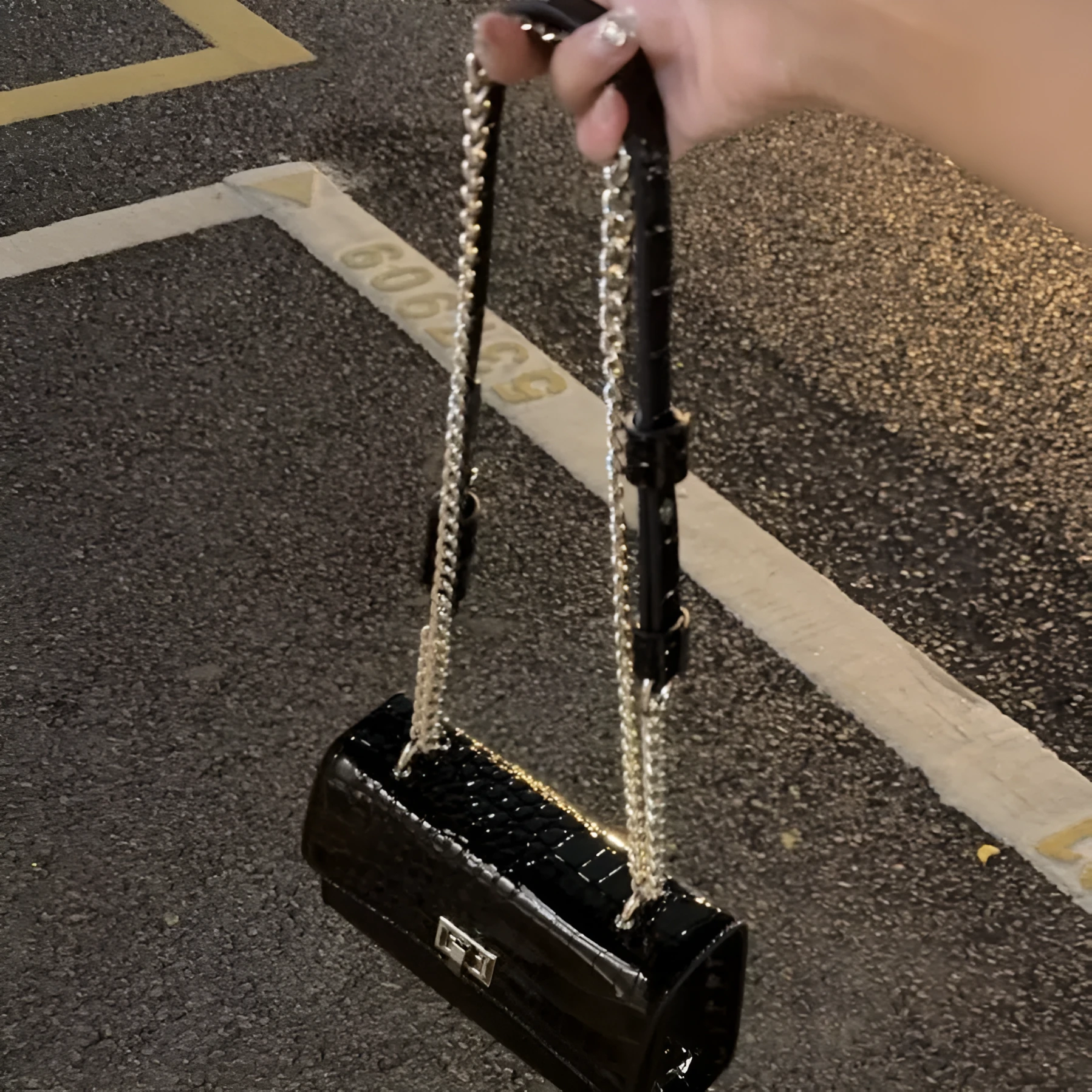 Black square crossbody bag with chain strap and bow tie detail on urban commuter setting
