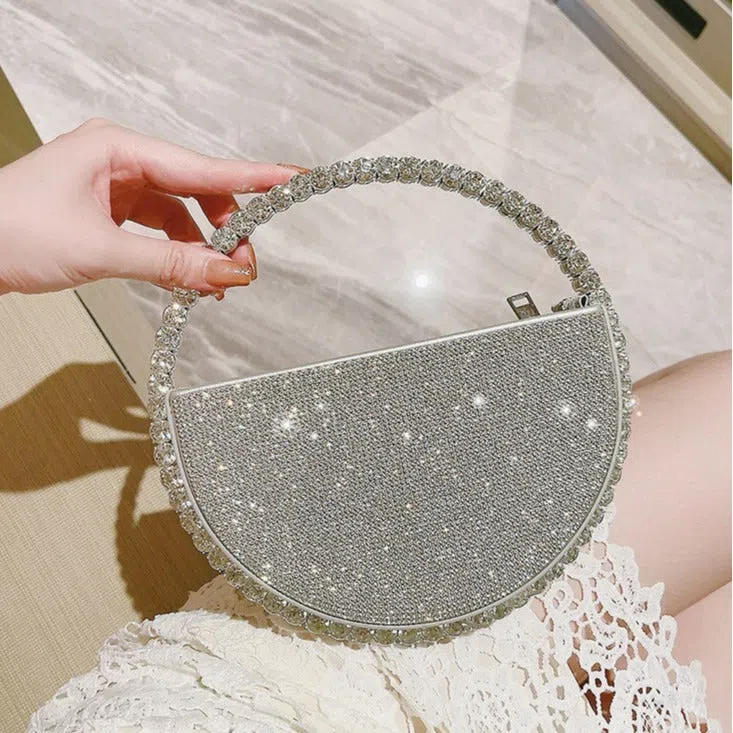 Round silver white PU evening bag with rhinestone details and crossbody strap on flat surface