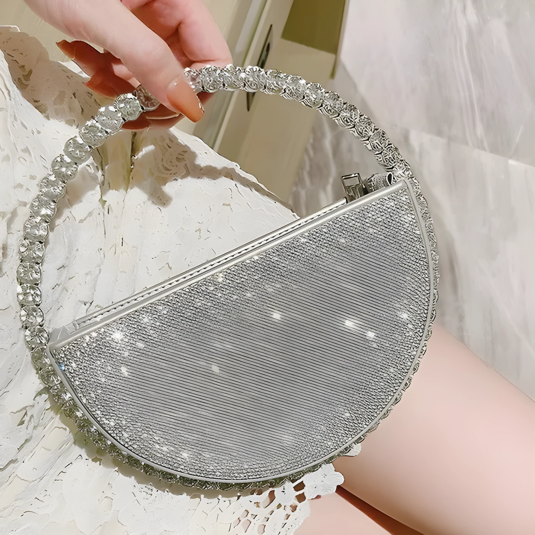 Round silver white PU evening bag with rhinestone details and crossbody strap on flat surface