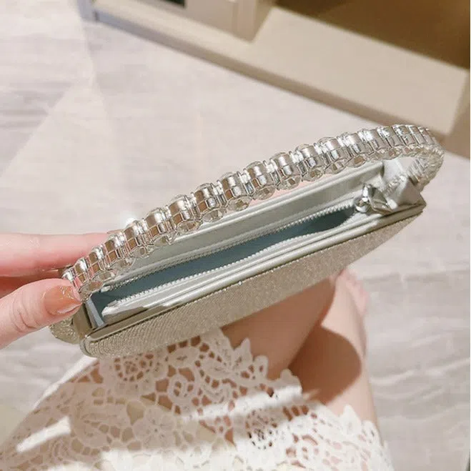 Round silver white PU evening bag with rhinestone details and crossbody strap on flat surface