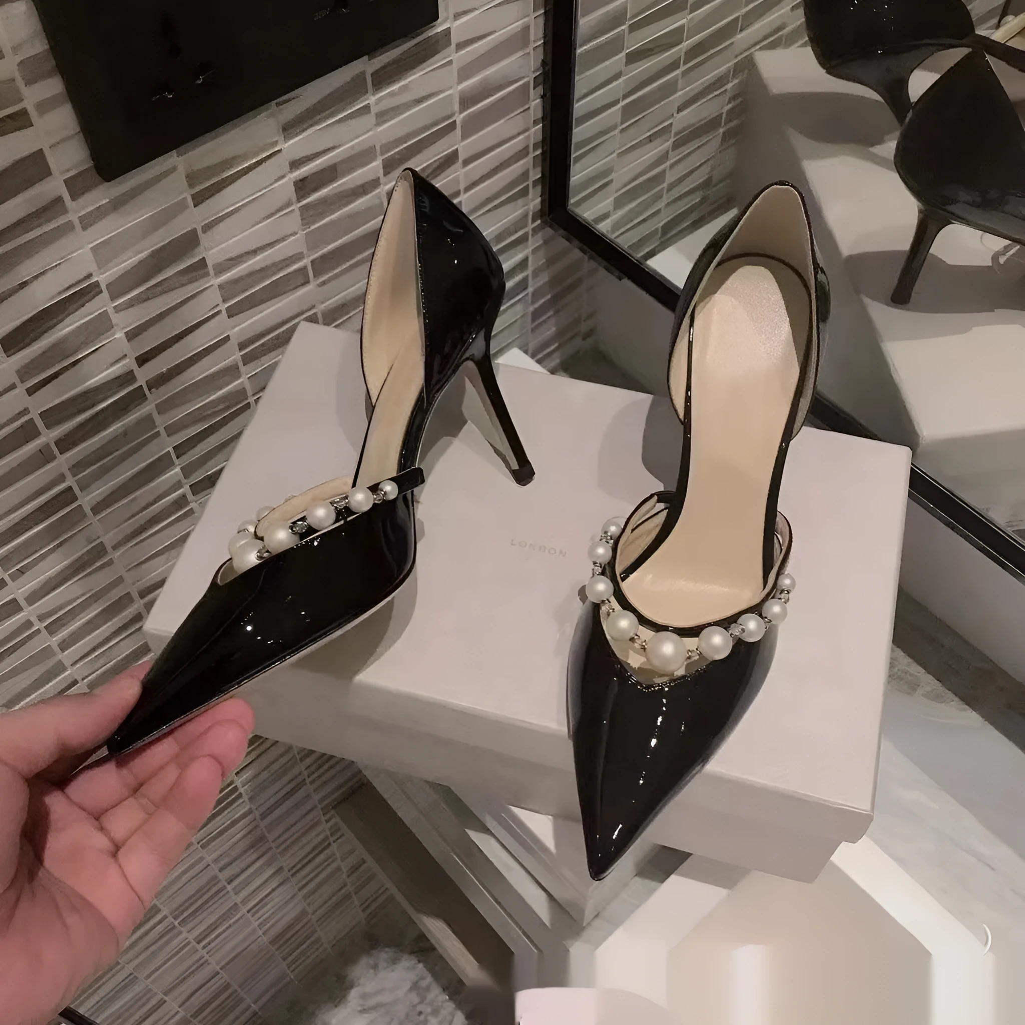 Black pointed toe patent leather women's stiletto heels with pearl decoration on the heel.