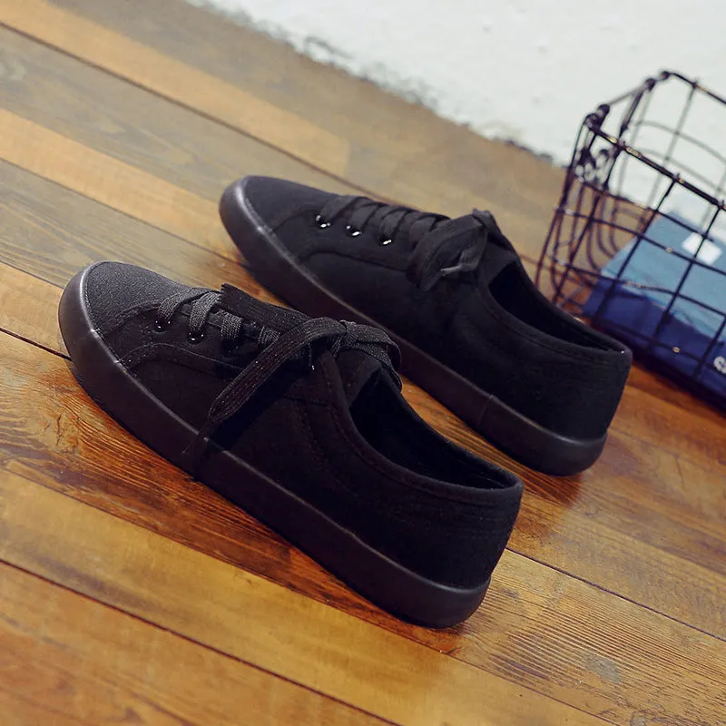 All black women's low-top canvas flat shoes with flat rubber sole and lace-up front.