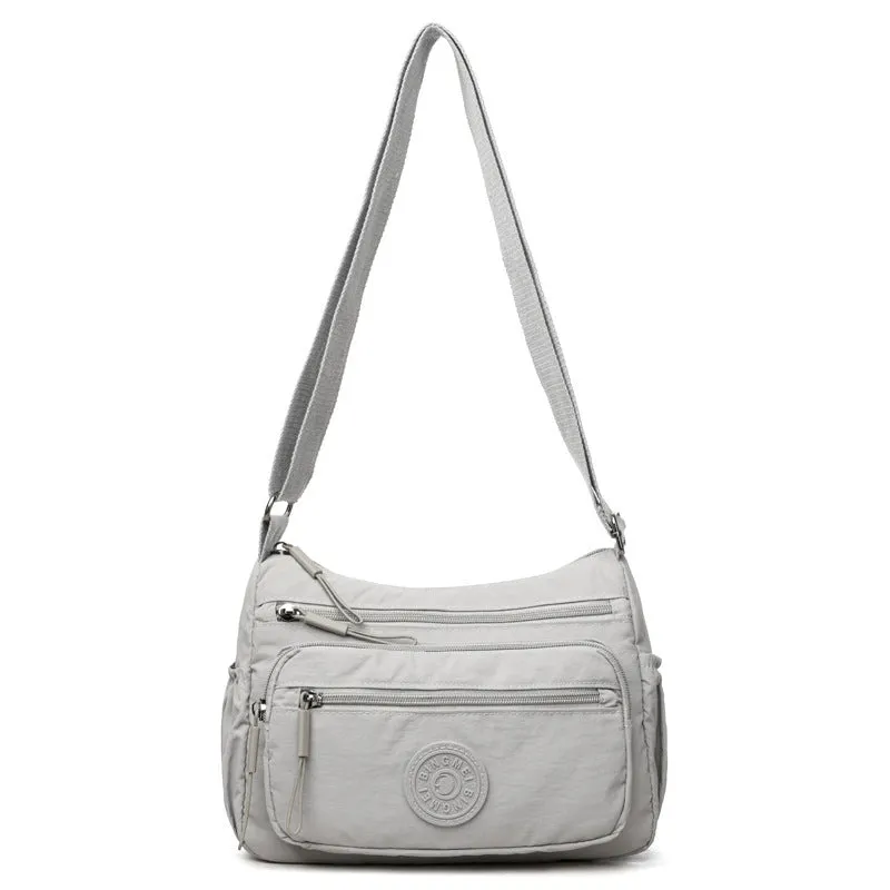 Soft water-repellent nylon crossbody bag in black, grey, or red, showing interior zipper pockets and an exterior 3D pocket.