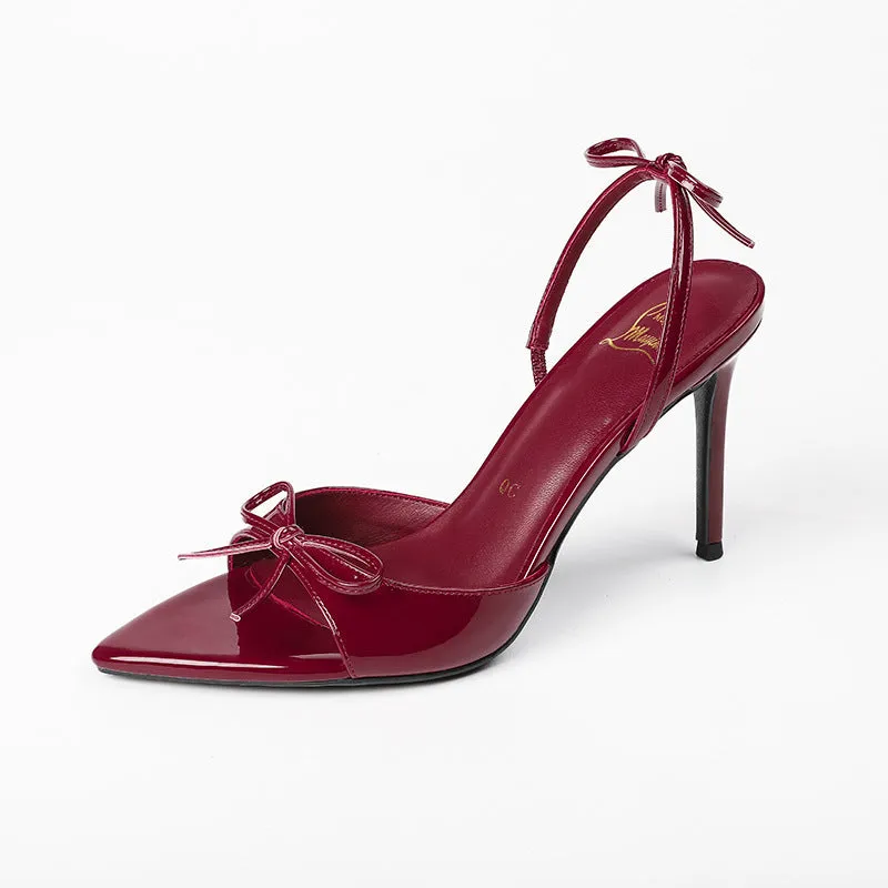 Black pointed stiletto high heels with open toe, ankle strap buckle, and a decorative bow on the upper.