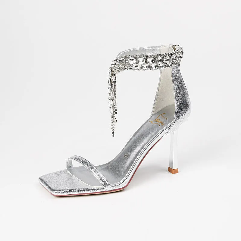 Women's silver high heel sandals with ankle buckle strap and square open toe on a plain background.