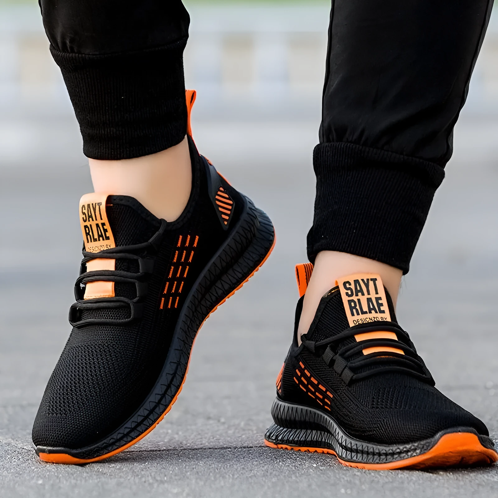 Men's low-top black casual trainers with cross-strap detail and flying weave upper, shown on a white background.