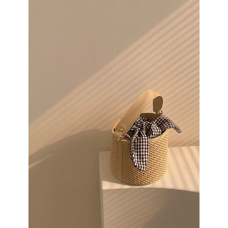 Women's medium beige PU bucket straw bag with open top and messenger strap on neutral background
