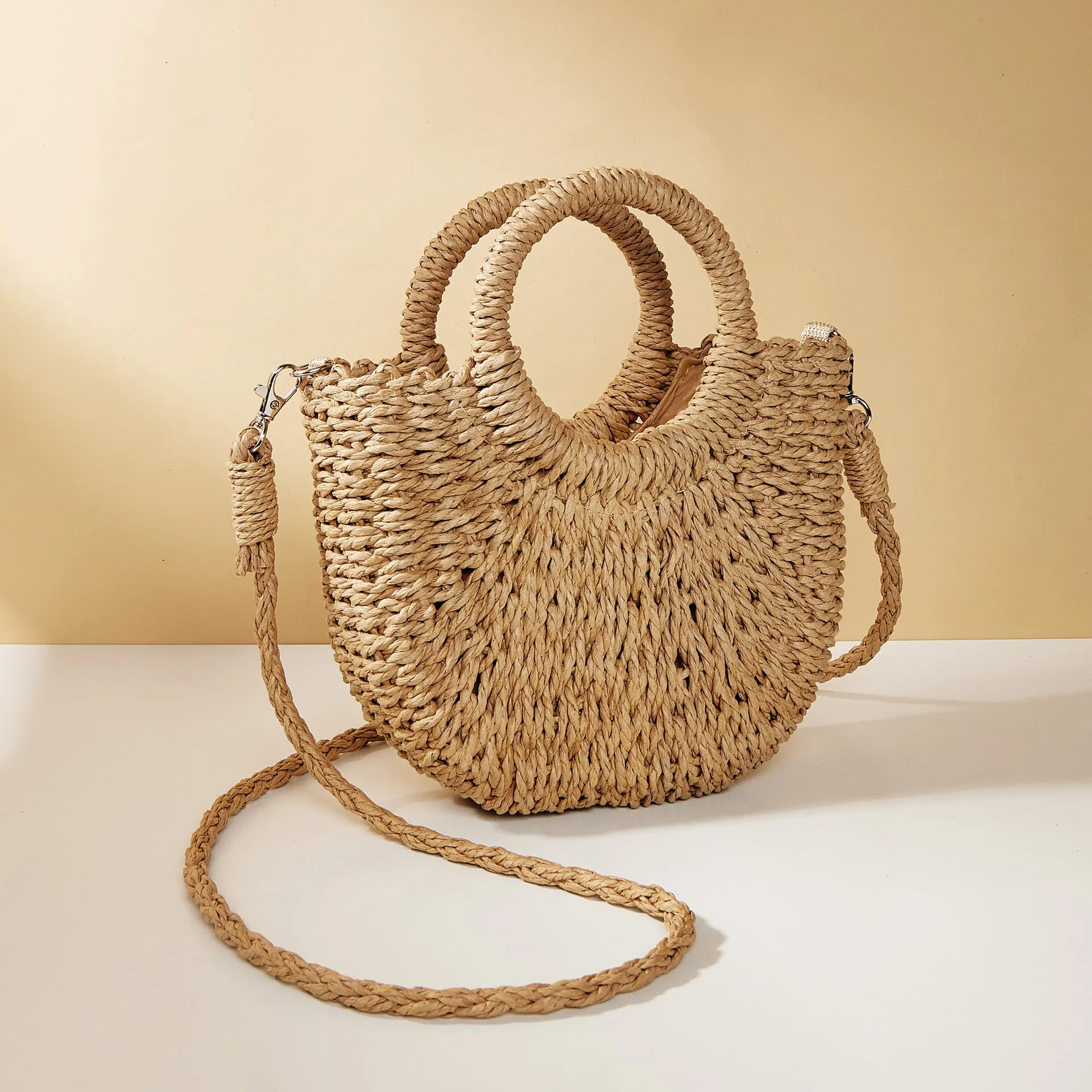 Woven straw beach bag in beige, peach skin lining, crossbody style, 24cm height, on a sandy beach