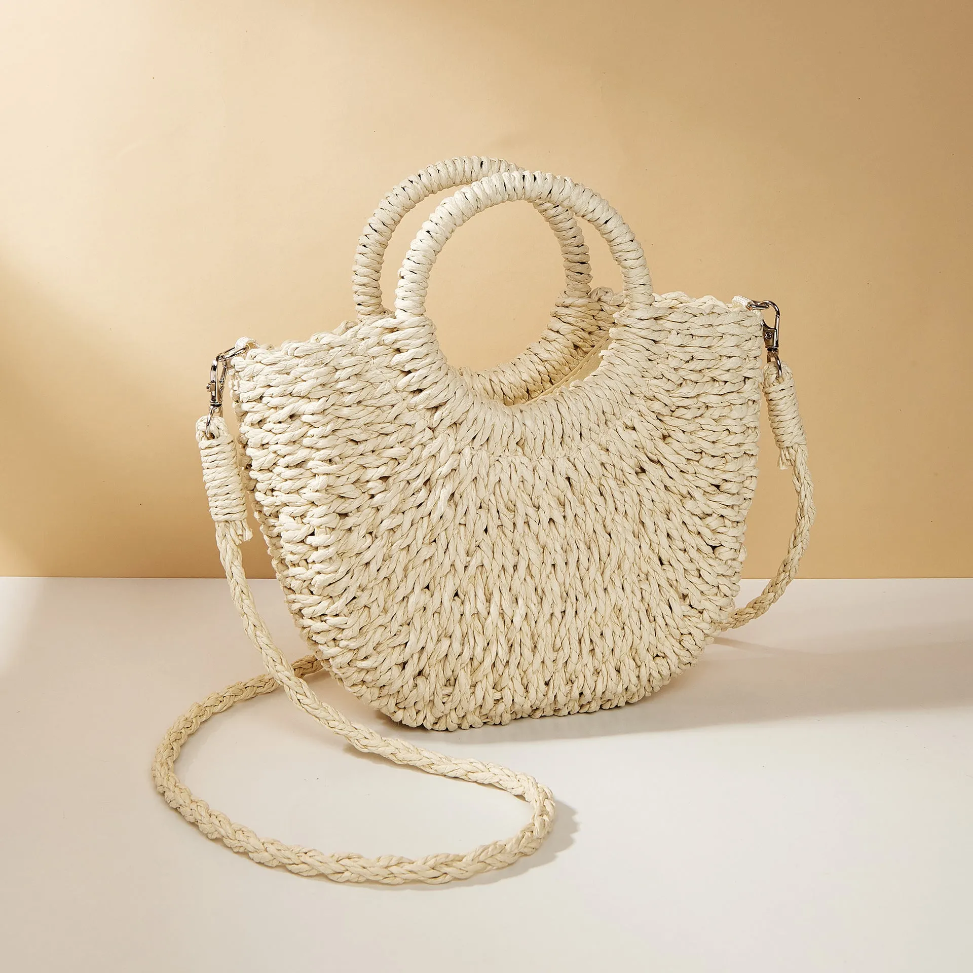 Woven straw beach bag in beige, peach skin lining, crossbody style, 24cm height, on a sandy beach