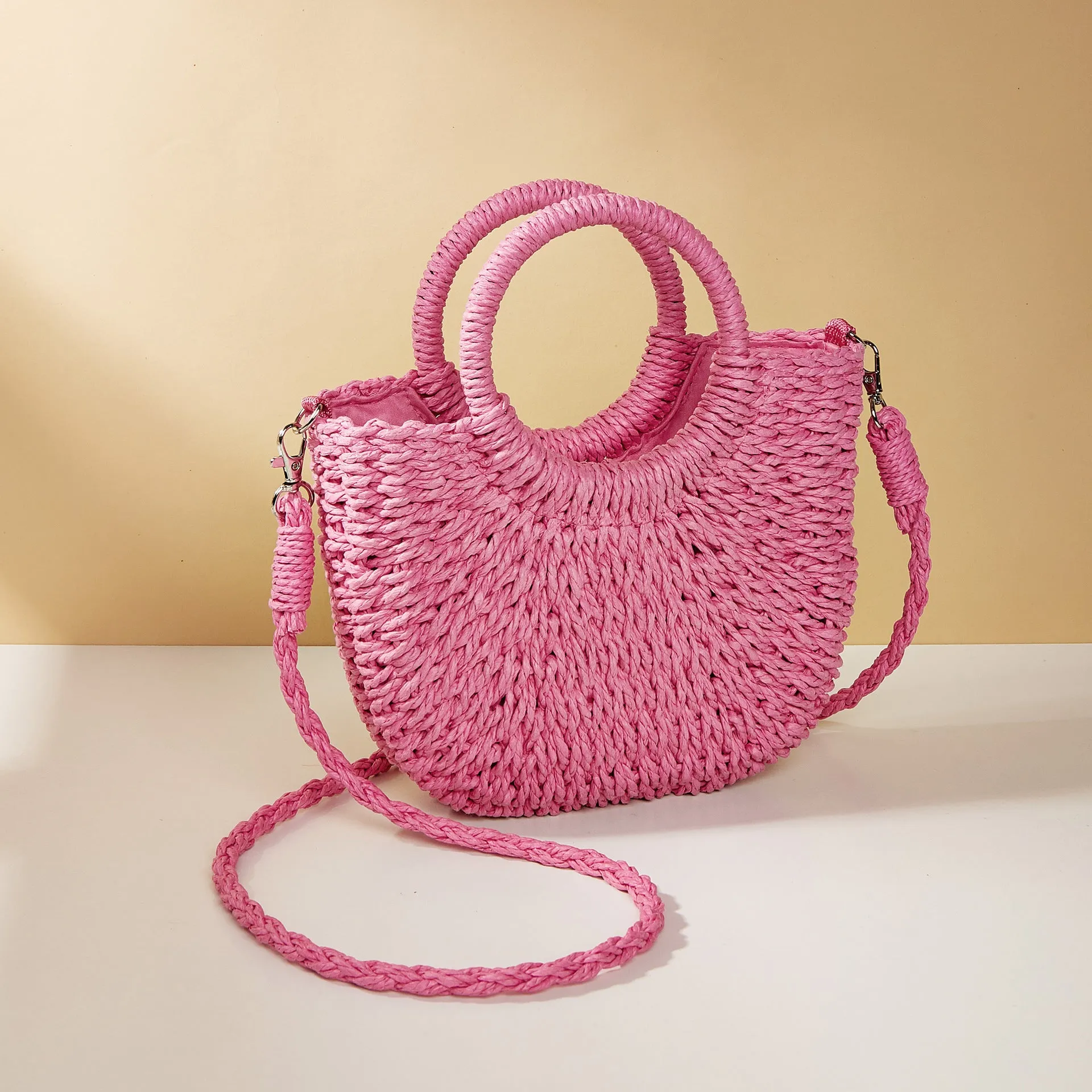 Woven straw beach bag in beige, peach skin lining, crossbody style, 24cm height, on a sandy beach