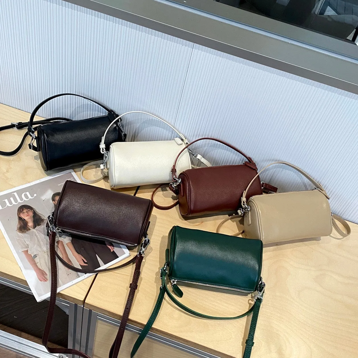 Cylindrical crossbody phone bag in soft genuine leather, shown in one of six colours including black or brown.