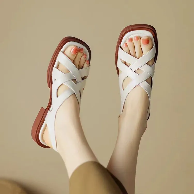 Women's black patent leather square toe sandals with a cross strap and low heel on a white background.