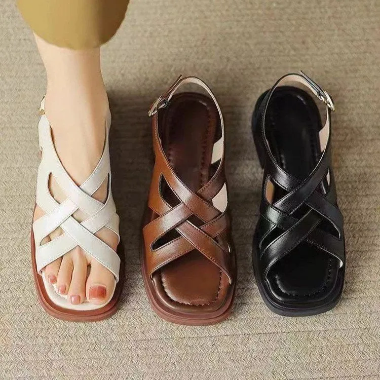 Women's black patent leather square toe sandals with a cross strap and low heel on a white background.