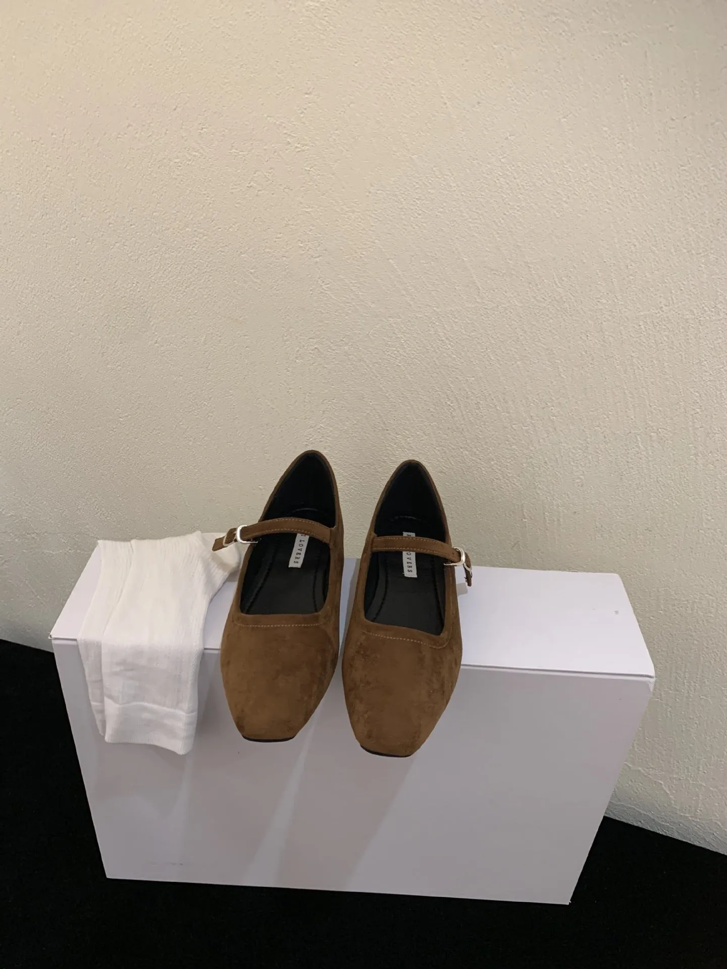 Women's black suede flat shoes with buckle closure and low heel on a neutral background