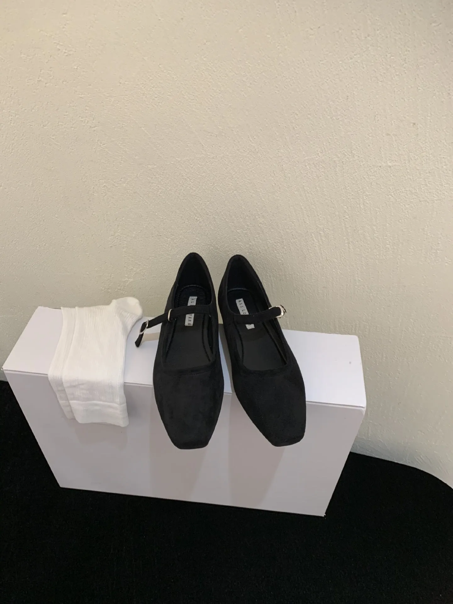 Women's black suede flat shoes with buckle closure and low heel on a neutral background