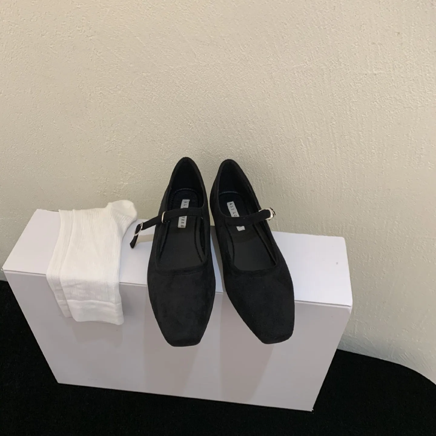 Women's black suede flat shoes with buckle closure and low heel on a neutral background