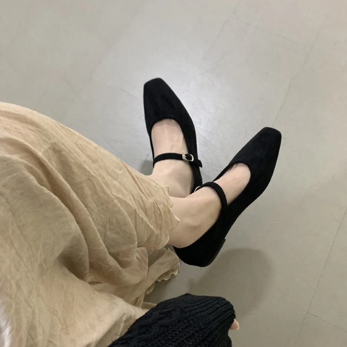 Women's black suede flat shoes with buckle closure and low heel on a neutral background