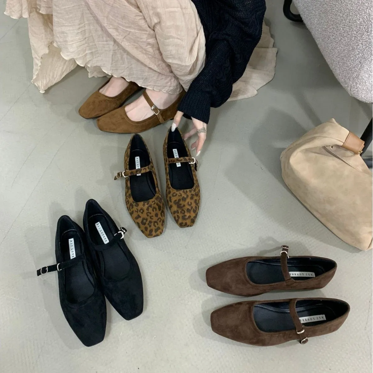 Women's black suede flat shoes with buckle closure and low heel on a neutral background