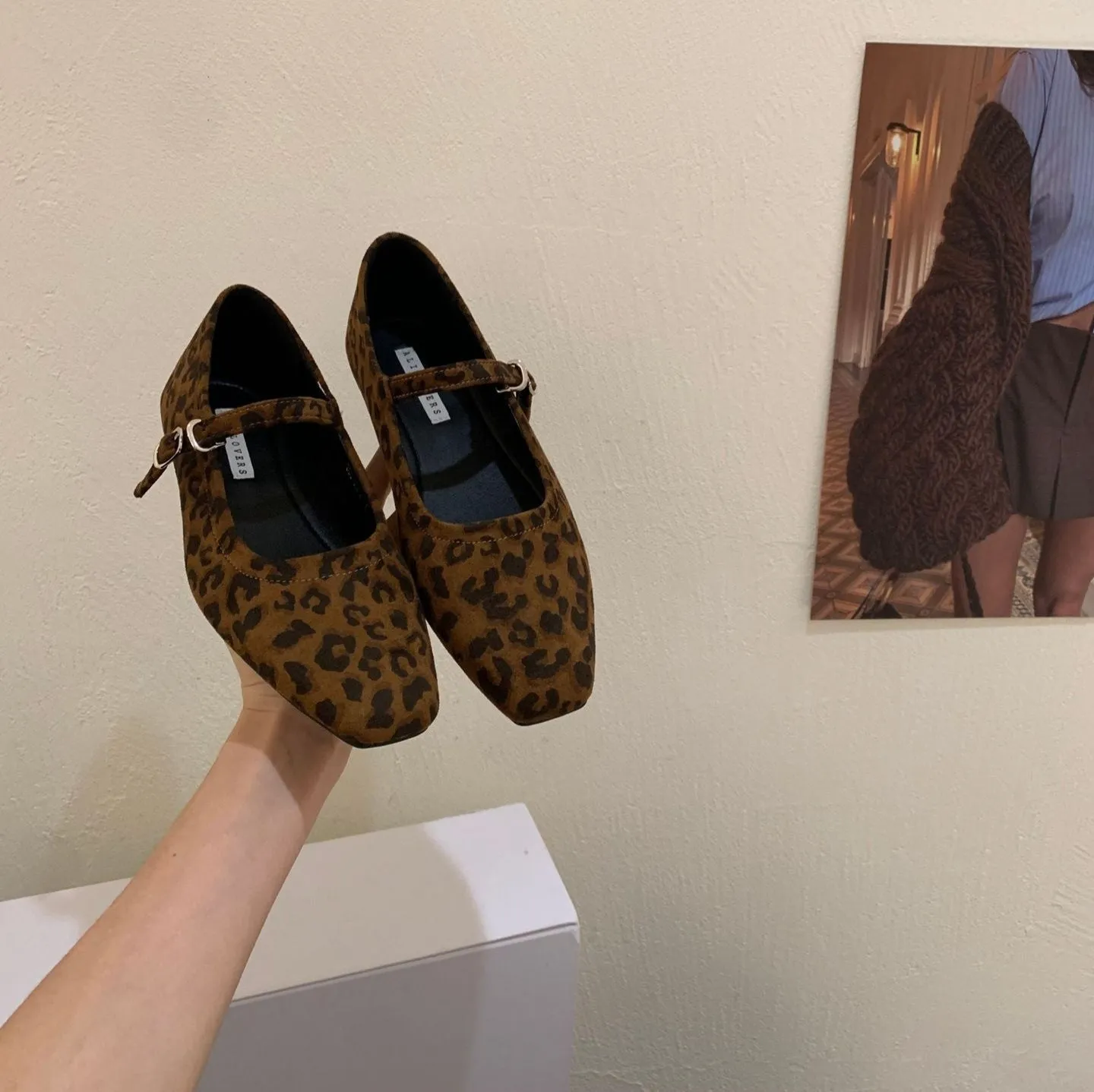 Women's black suede flat shoes with buckle closure and low heel on a neutral background