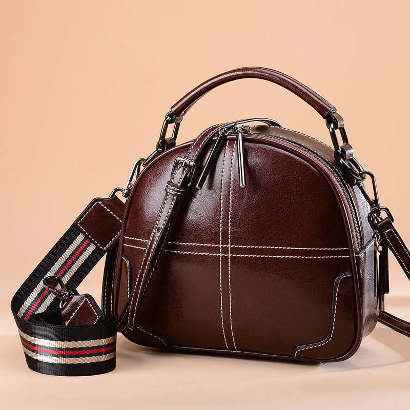 Round women's leather handbag with soft handles and a zip, shown in a choice of colours.