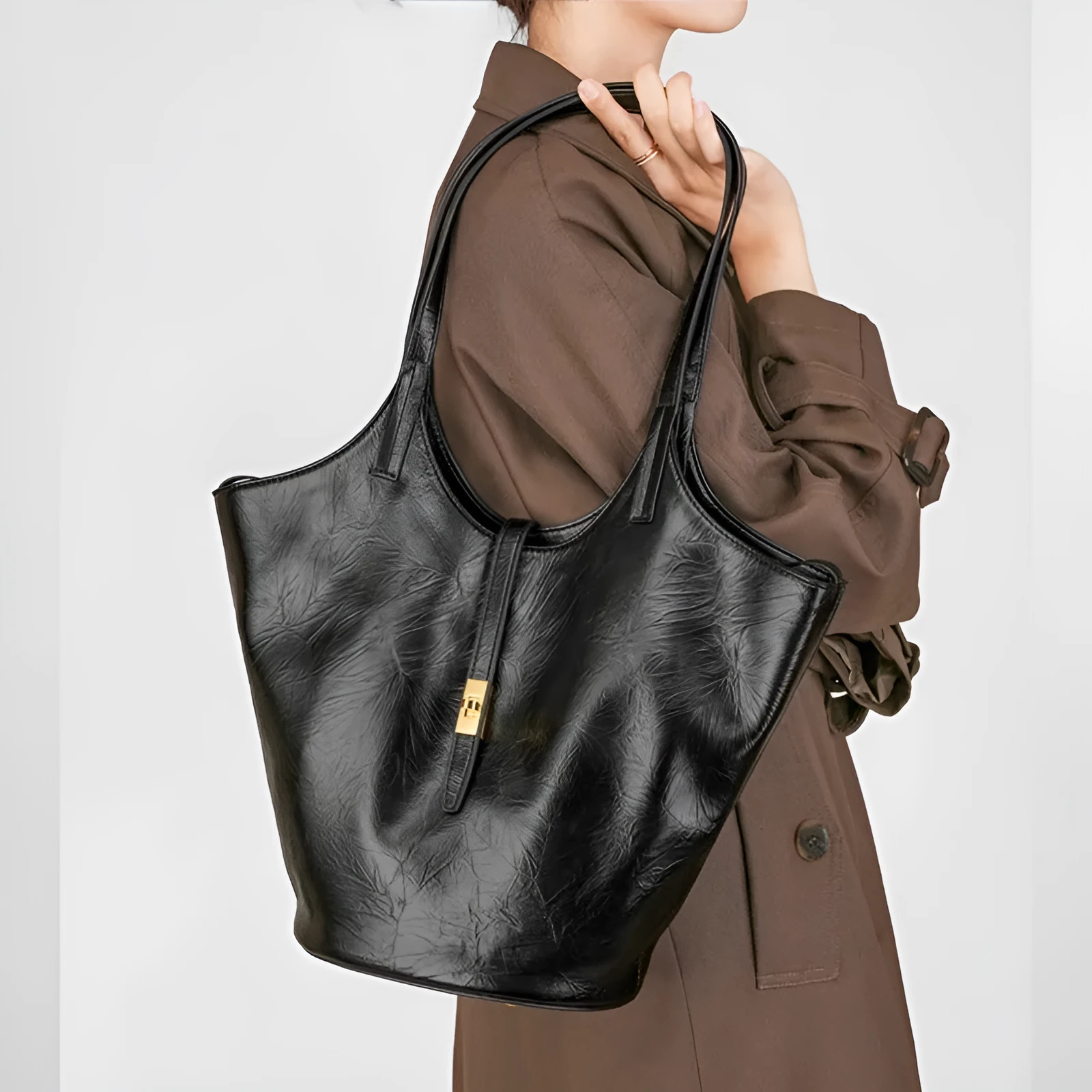 Black genuine leather bucket bag with visible sewing thread detail and crossbody strap on neutral background