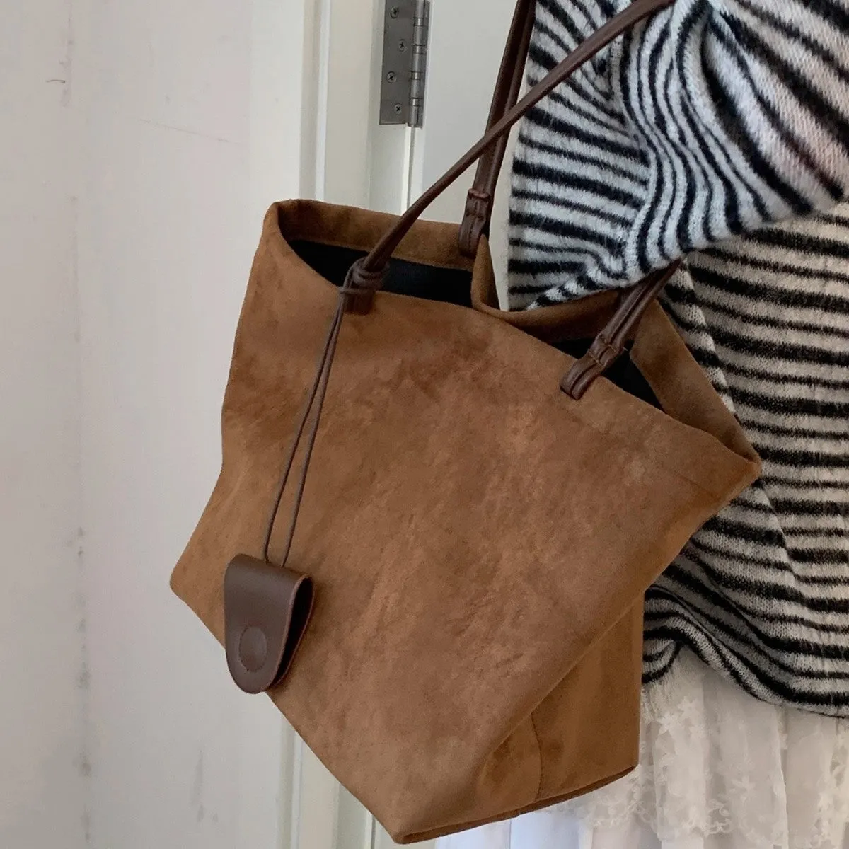 Brown suede shoulder bag with double straps and sewing line detail on a white background