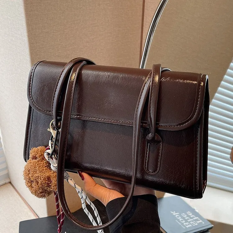 Brown women's square shoulder bag with pendant detail and adjustable crossbody straps on table
