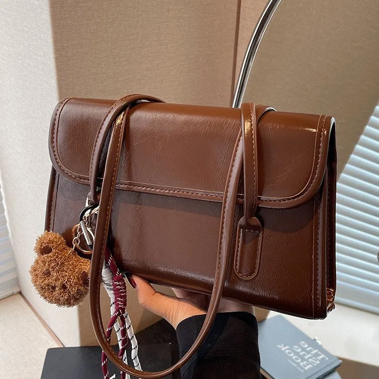 Brown women's square shoulder bag with pendant detail and adjustable crossbody straps on table