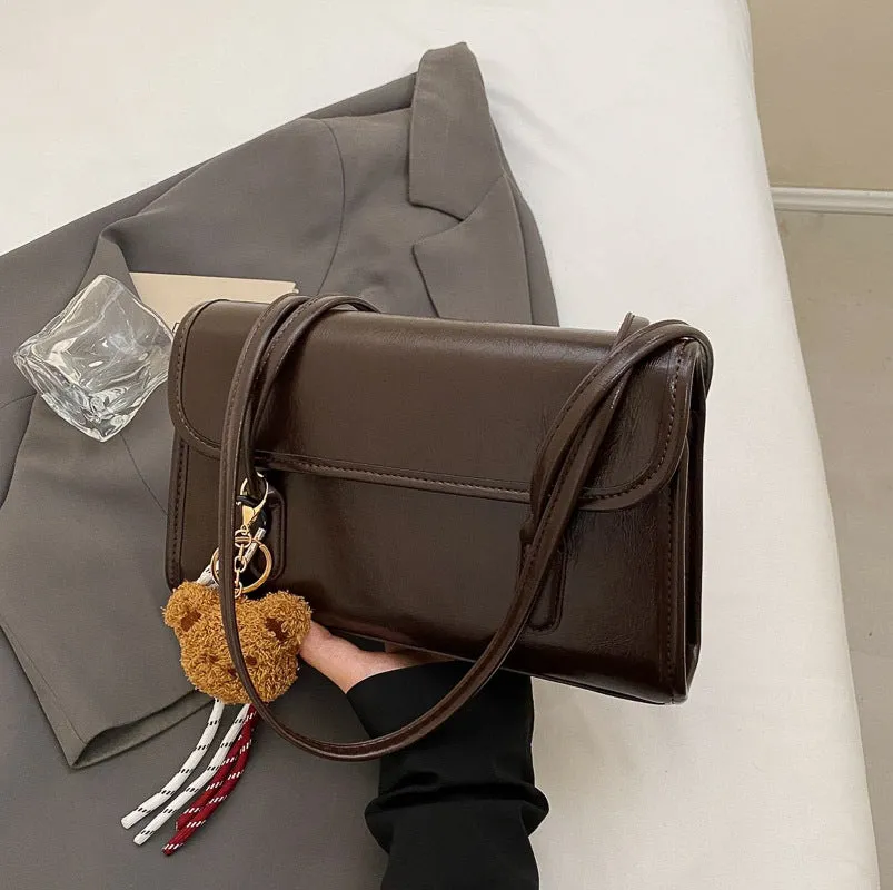 Brown women's square shoulder bag with pendant detail and adjustable crossbody straps on table