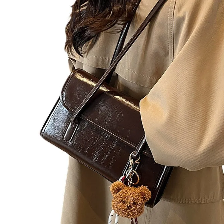 Brown women's square shoulder bag with pendant detail and adjustable crossbody straps on table