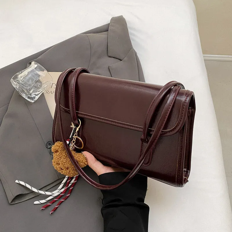 Brown women's square shoulder bag with pendant detail and adjustable crossbody straps on table