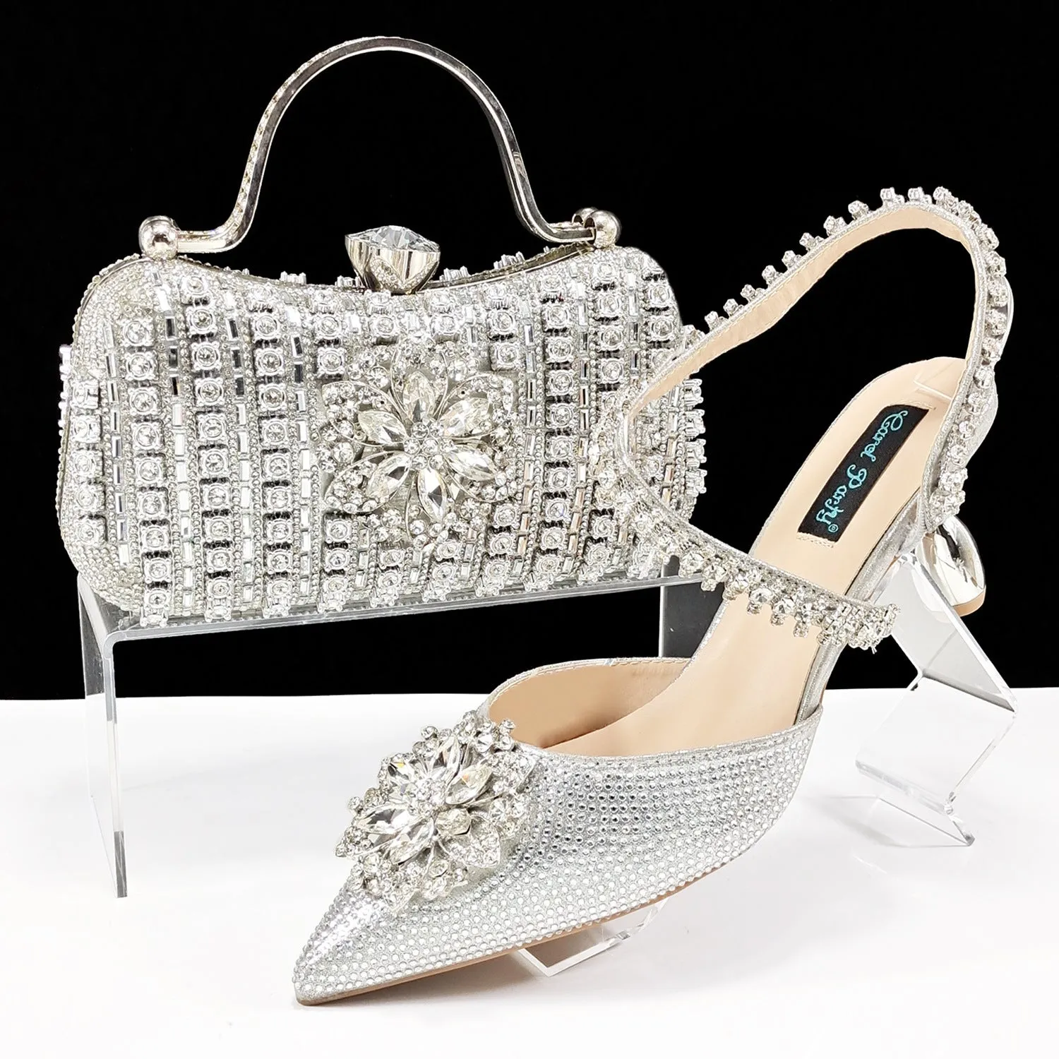 Women's black high-heel ankle strap sandal with rhinestone flower buckle and matching hard clutch bag.