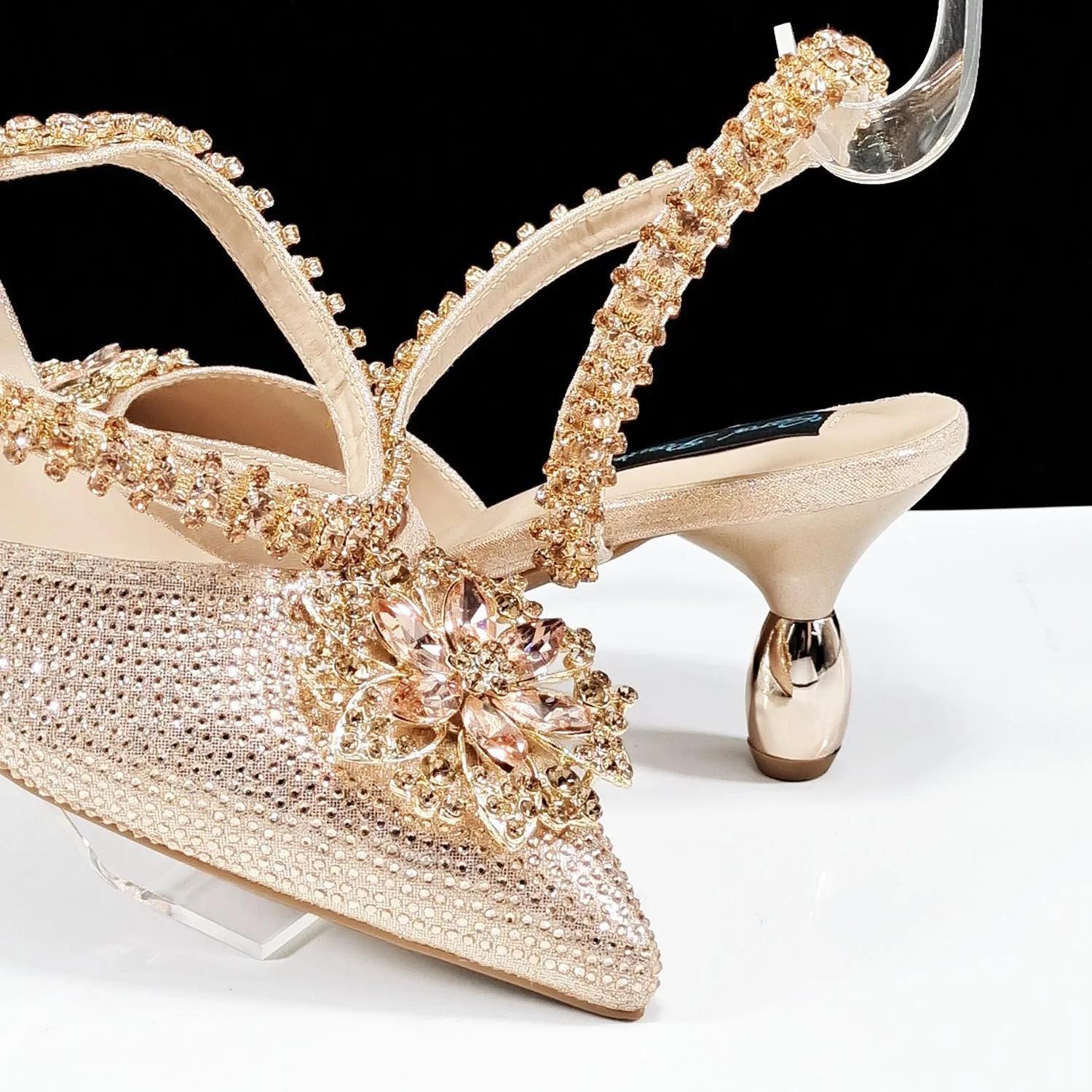 Women's black high-heel ankle strap sandal with rhinestone flower buckle and matching hard clutch bag.