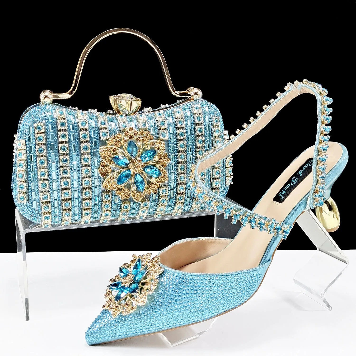 Women's black high-heel ankle strap sandal with rhinestone flower buckle and matching hard clutch bag.
