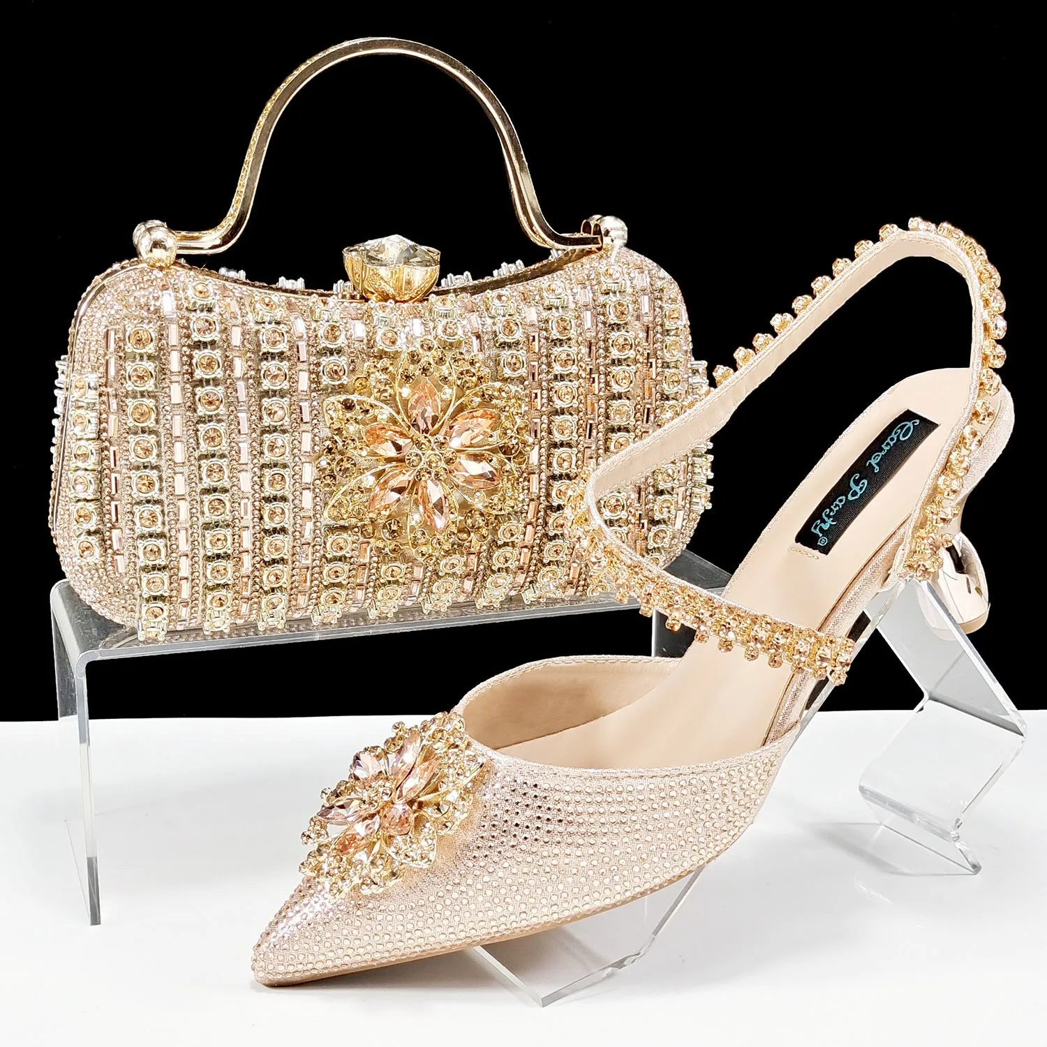 Women's black high-heel ankle strap sandal with rhinestone flower buckle and matching hard clutch bag.
