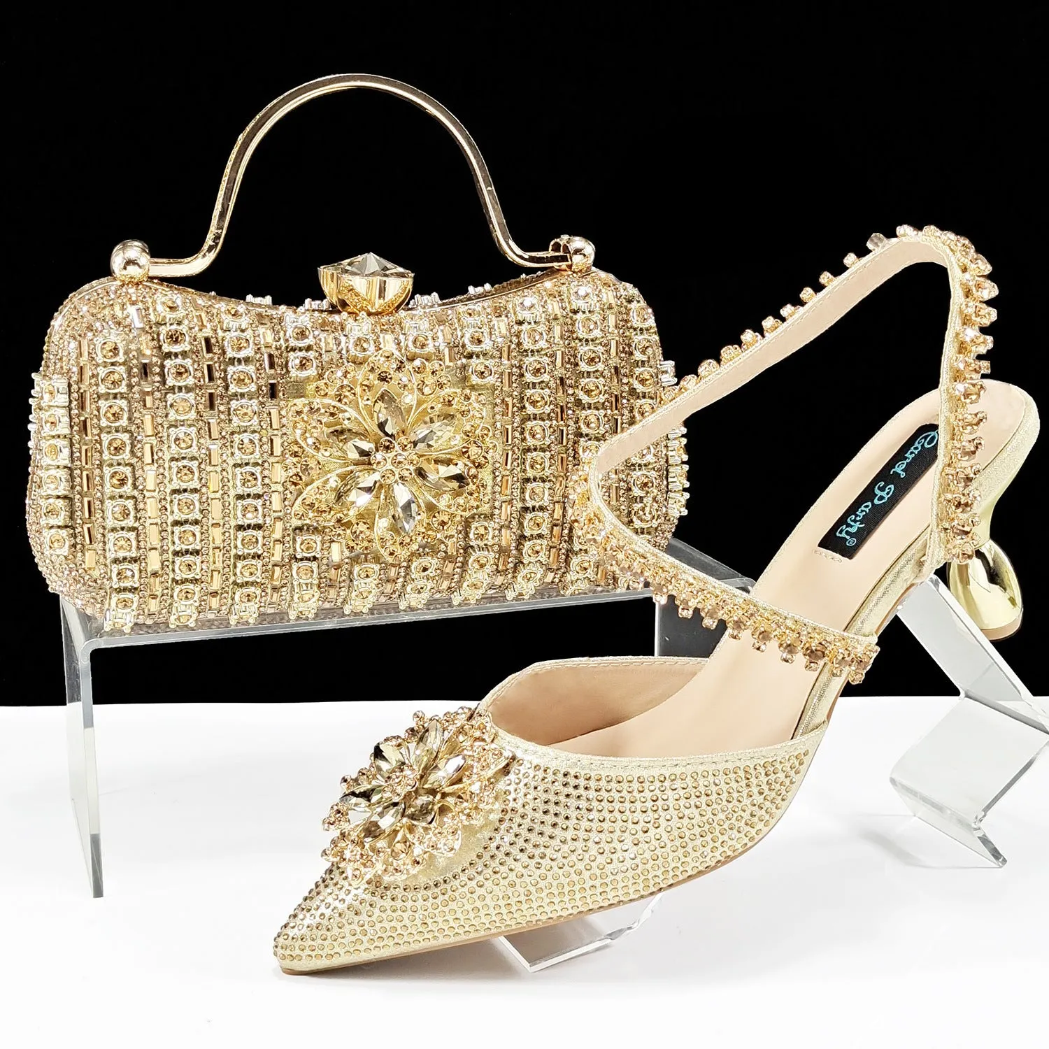 Women's black high-heel ankle strap sandal with rhinestone flower buckle and matching hard clutch bag.