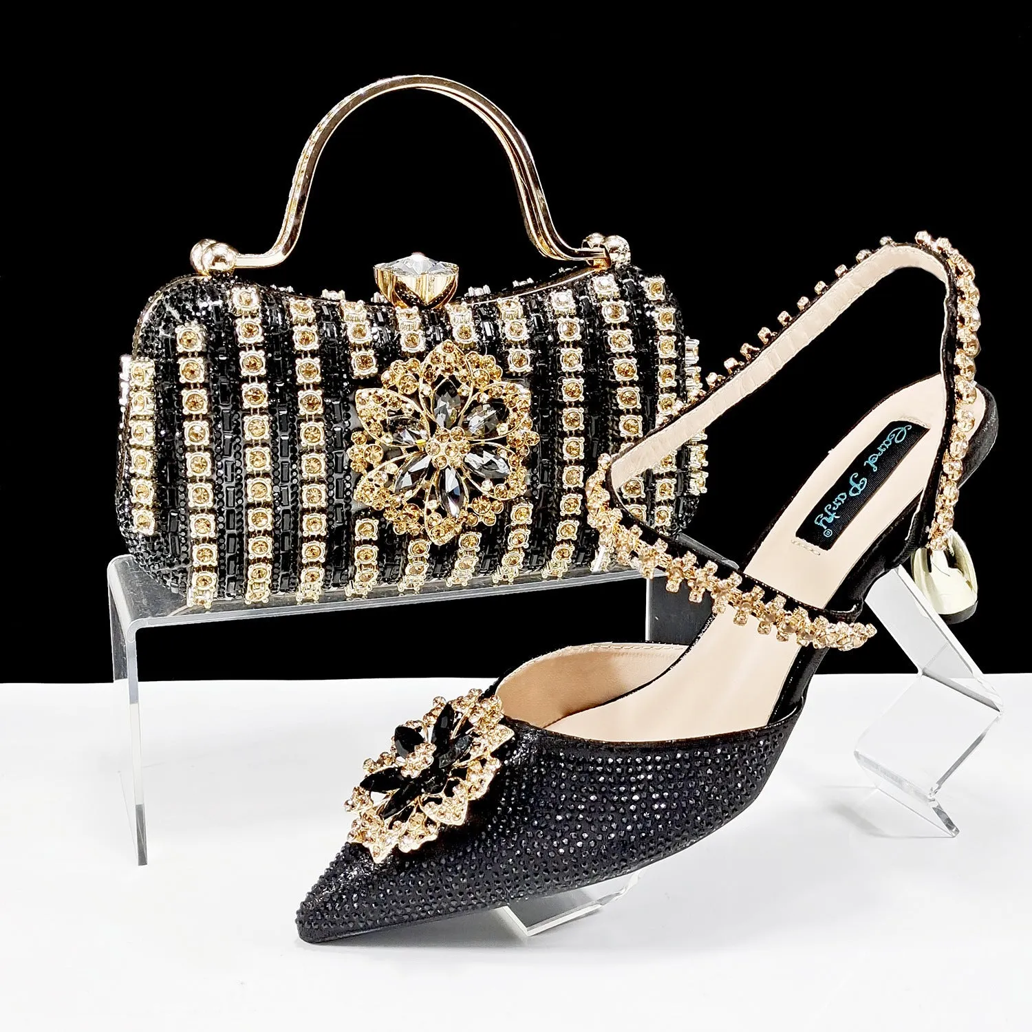 Women's black high-heel ankle strap sandal with rhinestone flower buckle and matching hard clutch bag.