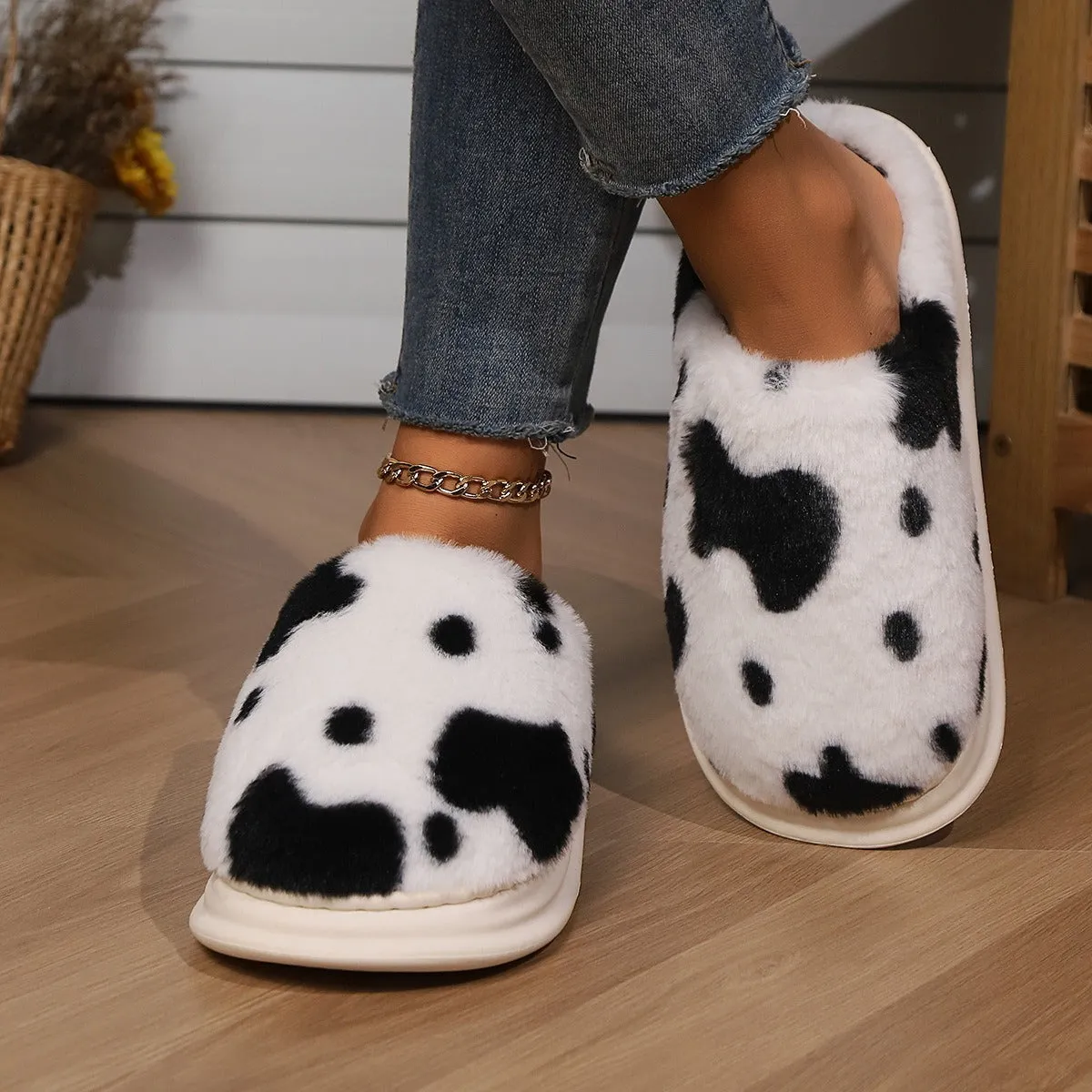 Cow spotted plush slippers in brown with round toe and baotou style on a home floor