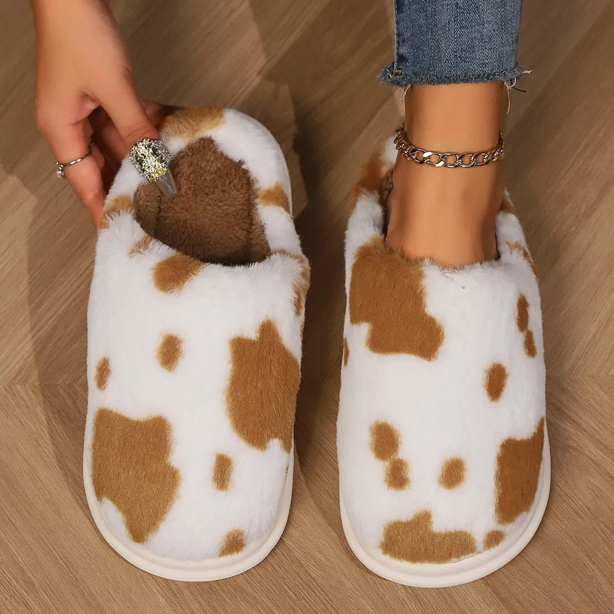 Cow spotted plush slippers in brown with round toe and baotou style on a home floor