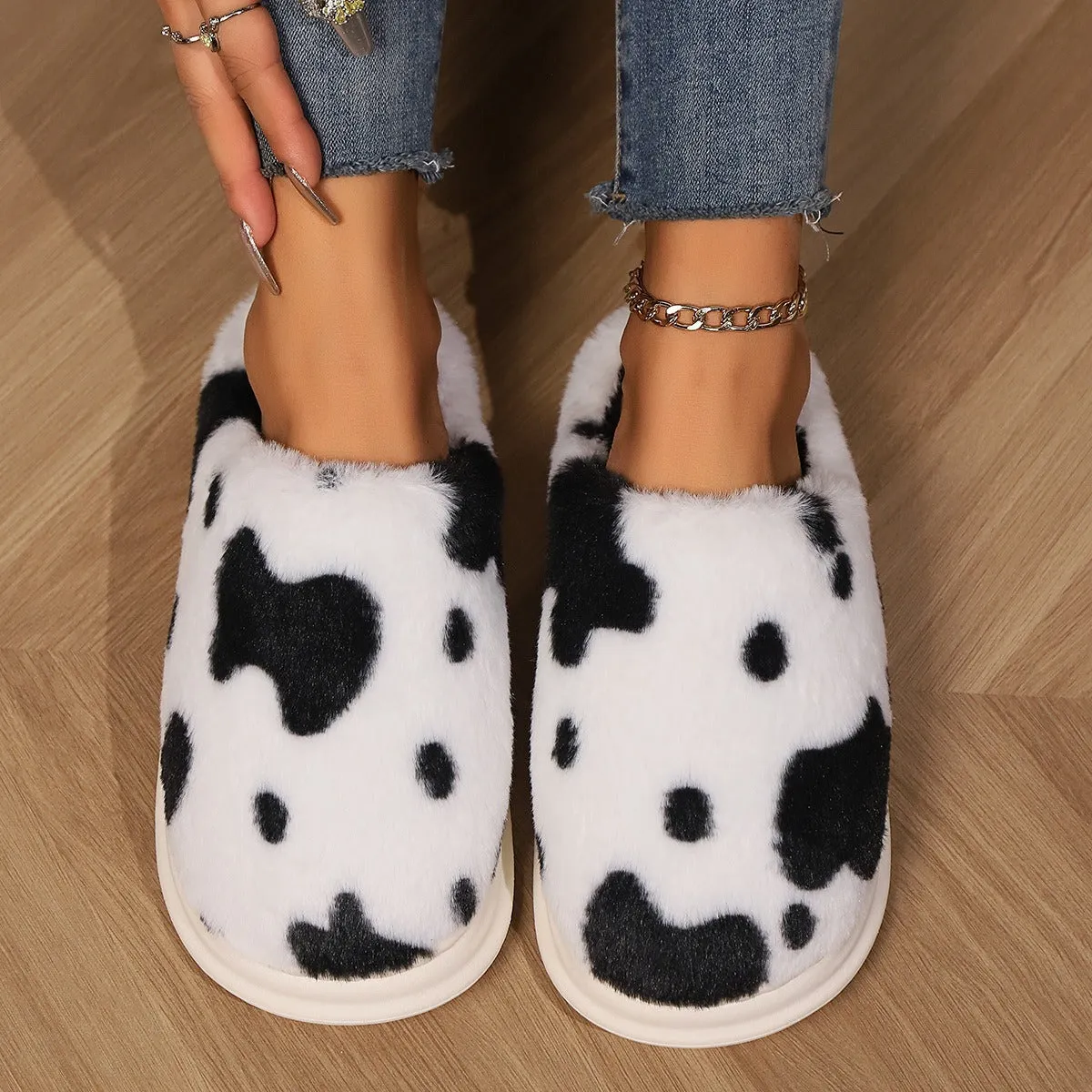 Cow spotted plush slippers in brown with round toe and baotou style on a home floor